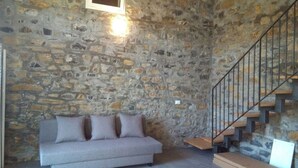 Una habitación con pared de piedra, un sofá gris y una escalera con barandilla de metal.