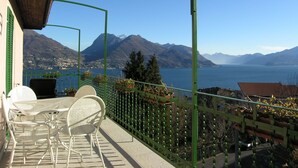 Un balcón con mobiliario exterior, vista a un lago, montañas y cielo despejado.