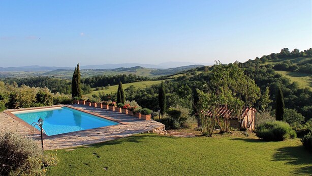 Una piscina rectangular con solárium de piedra, rodeada de un paisaje verde exuberante y colinas a lo lejos.