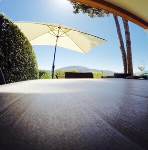 Une terrasse extérieure avec une table, un grand parasol et un verre à vin.