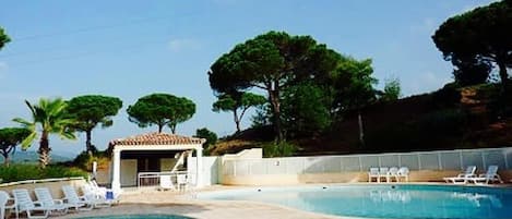 A swimming pool with lounge chairs, a small pavilion, and trees in the background.