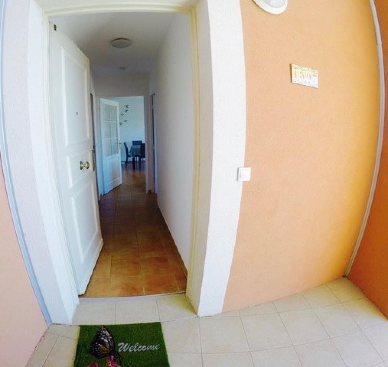 Un couloir étroit, avec un paillasson à l’entrée, qui mène à une pièce dotée d’une porte et d’un interrupteur sur le mur.