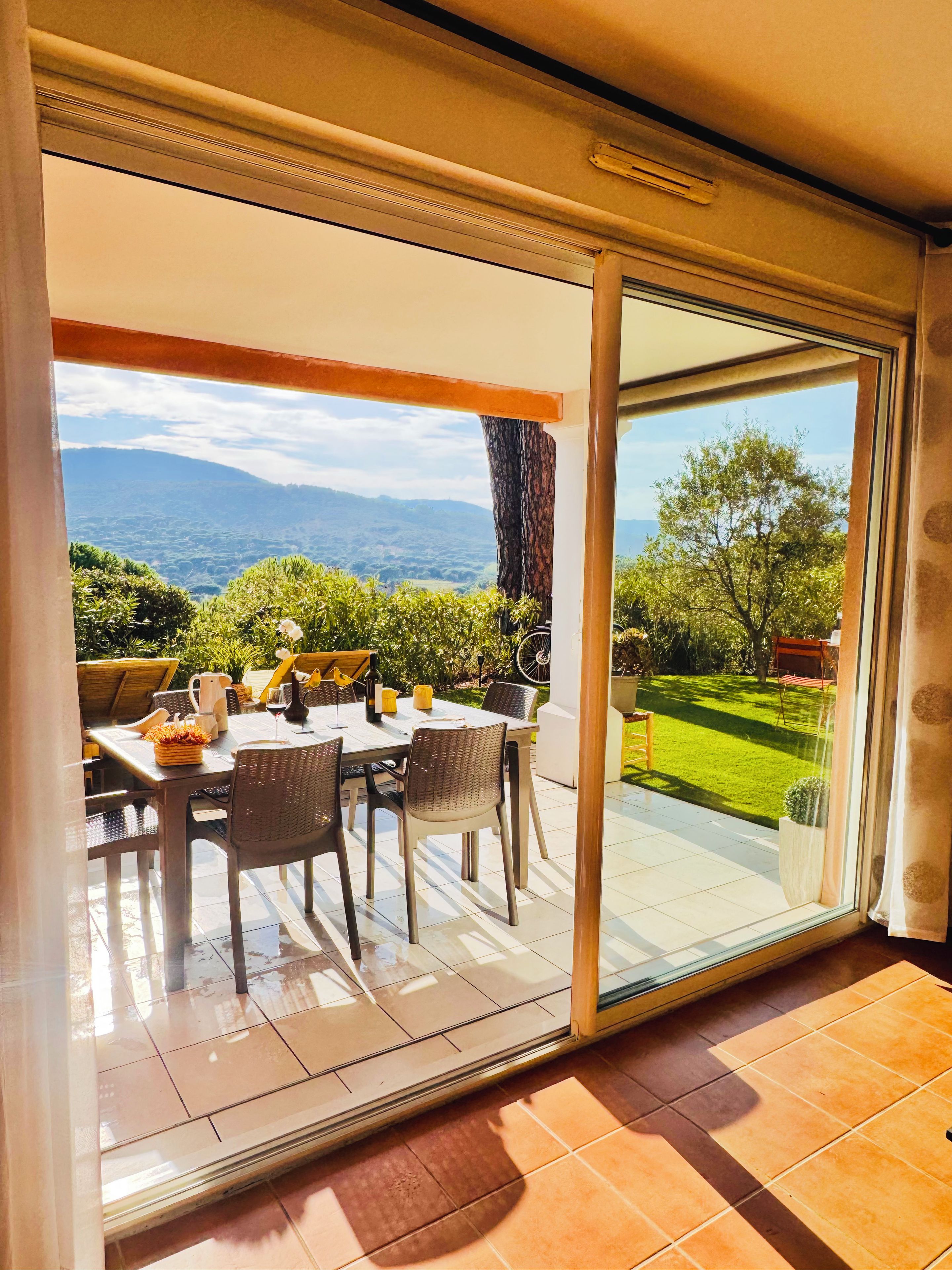 A dining area with a table set for two, a view of a lush garden, and a mountain landscape in the background.