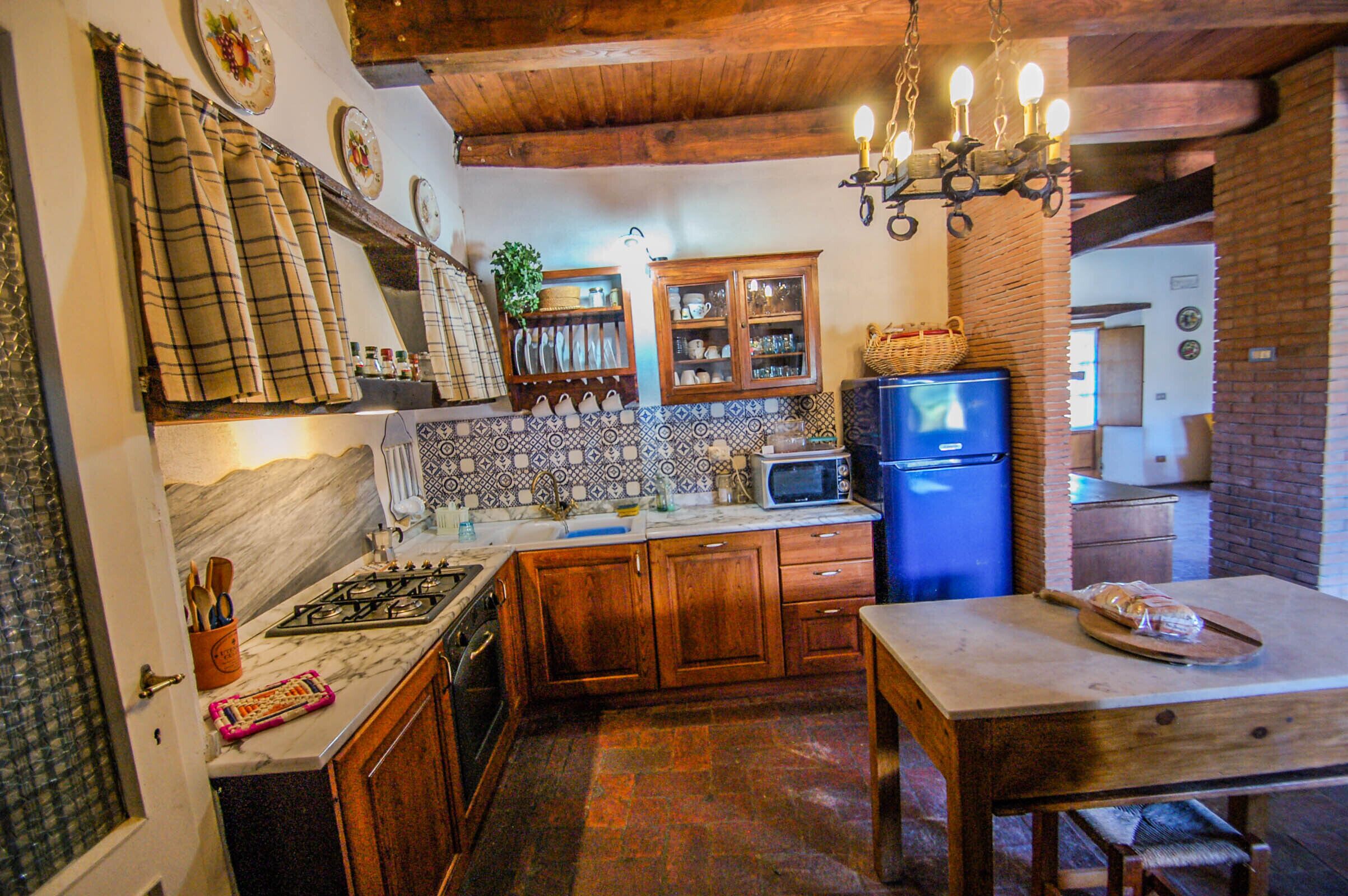 A kitchen with wooden cabinets, a marble countertop, a blue refrigerator, and a chandelier.