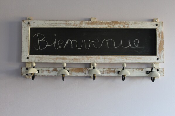 Een schoolbord waarop het woord 'Bienvenue' staat geschreven, gemonteerd in een rustieke witte houten lijst met daaronder een reeks witte belletjes.