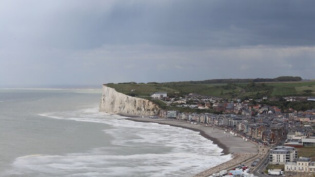 Une ville côtière caractérisée par une falaise imposante, une plage et une zone densément bâtie avec des immeubles le long du littoral.