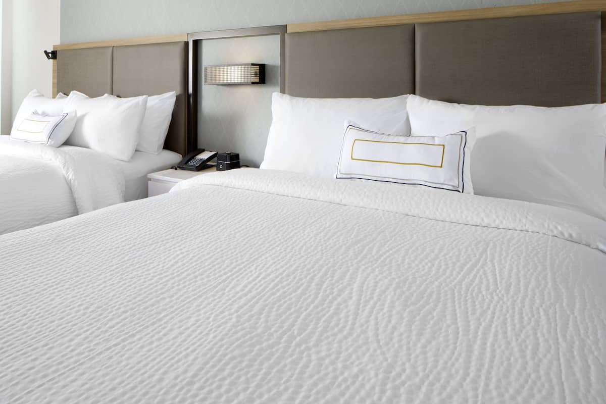 A hotel room with two beds, a nightstand with a phone, and a wall-mounted light fixture.