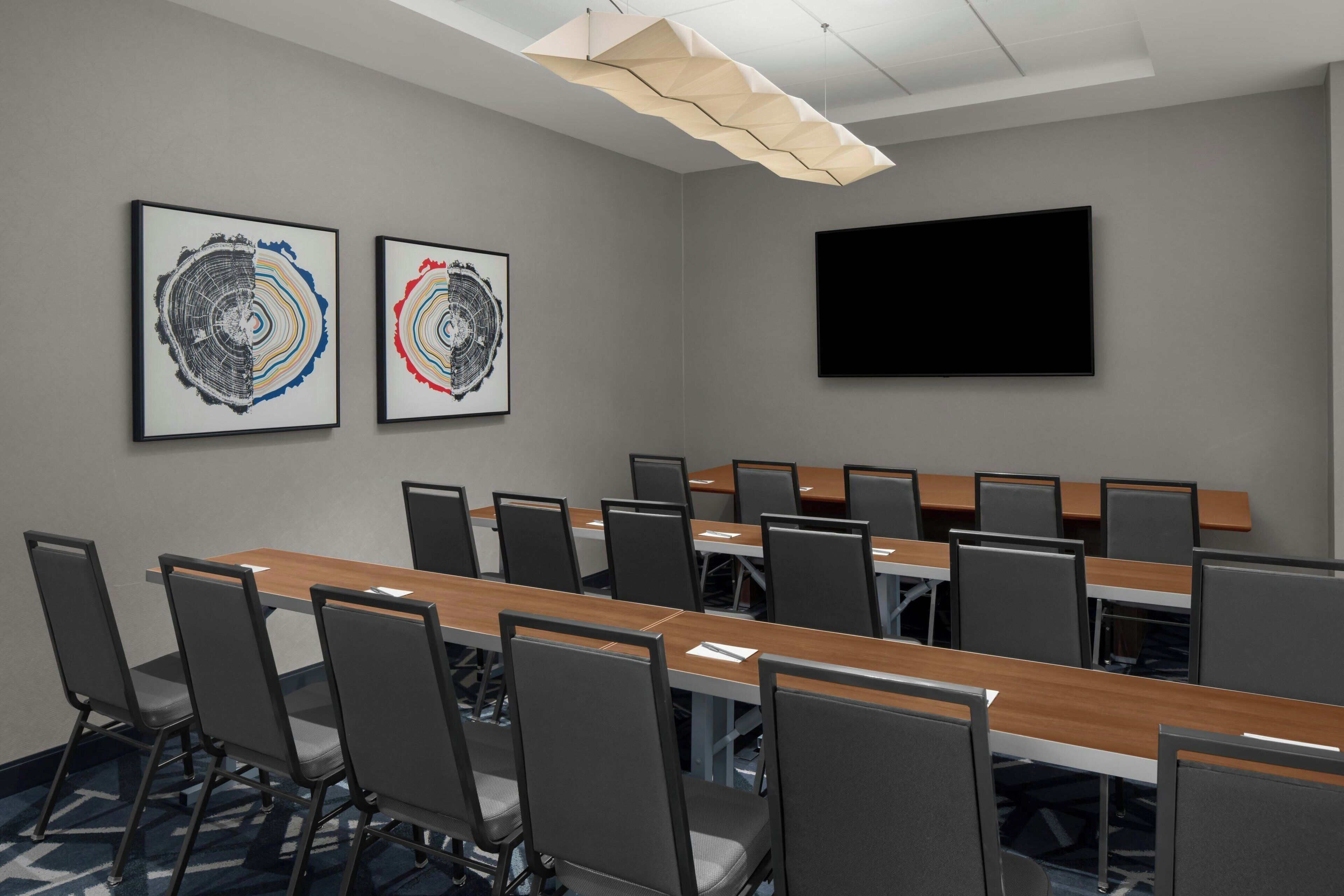 Une salle de conférence avec une longue table, de nombreuses chaises, deux œuvres d’art encadrées et un téléviseur à écran plat.