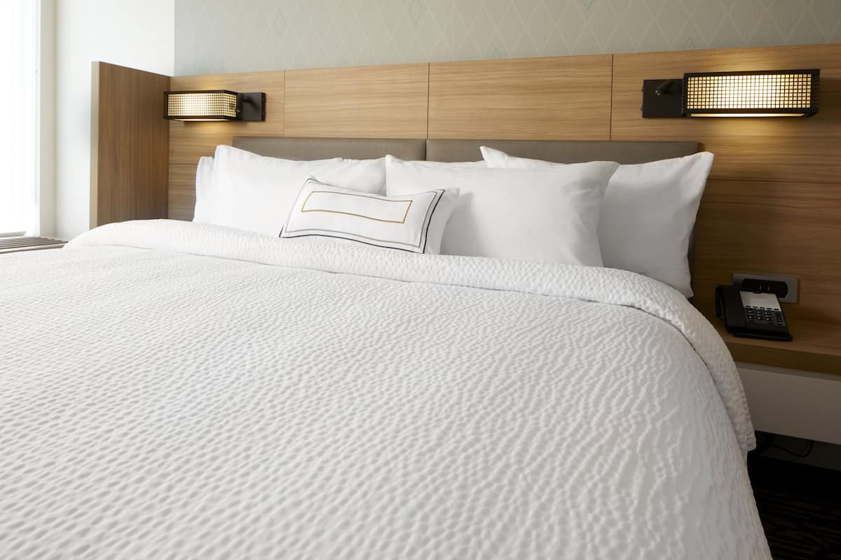 A hotel room with a neatly made bed, a wooden headboard, two wall-mounted lamps, and a telephone on the nightstand.