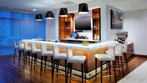 A modern kitchen with a long island counter, bar stools, a flat-screen TV, and a coffee machine.