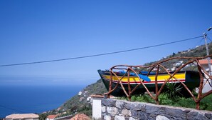 A coastal view with a colorful boat resting on a stone wall, overlooking the sea. - Casa do Barco, Rustic house with salt pool and sea view (Arco da Calheta)