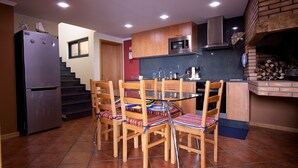 A compact kitchen with a refrigerator, microwave, and a wood-fired oven. There are four wooden chairs with striped cushions around a glass table. - Casa do Barco, Rustic house with salt pool and sea view (Arco da Calheta)