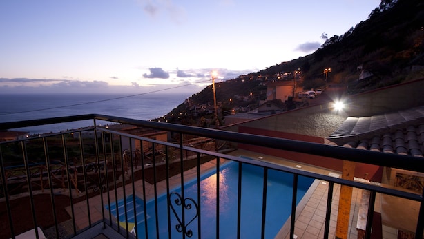 A balcony with a pool, overlooking a coastal town with houses and a view of the sea. - Casa do Barco, Rustic house with salt pool and sea view (Arco da Calheta)