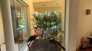 Ein Zimmer mit Glastür und Zugang zu einem Balkon mit Blick auf einen Garten und einen Baum.