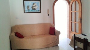A beige sofa with red cushions, a framed picture of sailing ships on the wall, and a wooden door with glass panels.