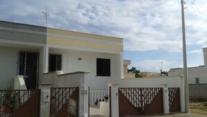 A modern two-story house with a gated entrance, a small balcony, and a clear sky.