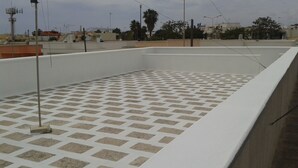 A rooftop with a patterned floor, surrounded by buildings and a clear sky.