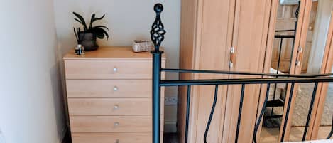 A bedroom with a wooden dresser, a bed with a white blanket, and a wooden wardrobe.