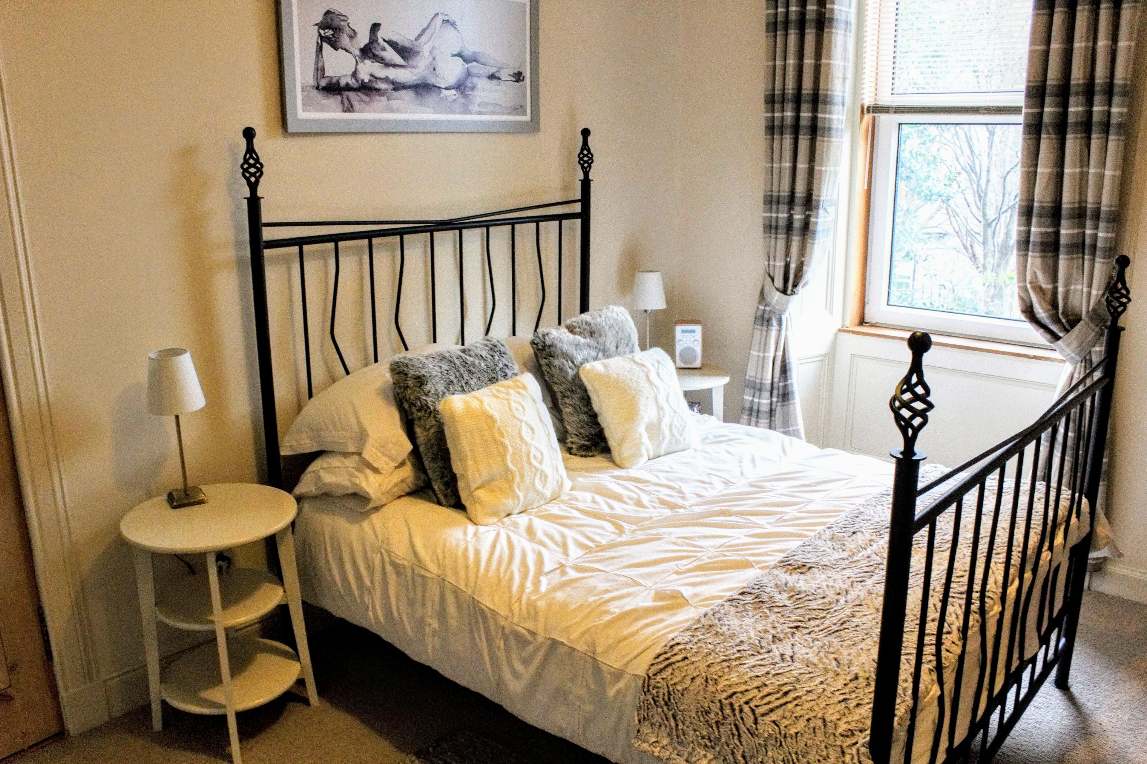 A bedroom with a bed, bedside tables, a lamp, a painting on the wall, and a window with curtains.