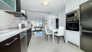 Una cocina moderna con electrodomésticos de acero inoxidable, un comedor con sillas blancas y vistas a la ciudad.