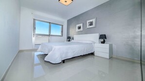 Un dormitorio moderno con una cama grande, una mesita de noche y una ventana que ofrece vistas al cielo.