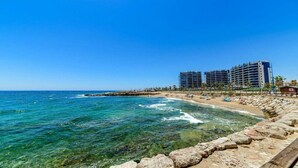 Un hotel frente al mar con varios edificios altos, un litoral rocoso y aguas azules cristalinas.