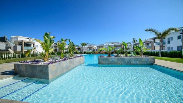 Piscina con agua azul cristalina, rodeada de edificios modernos y abundante vegetación.