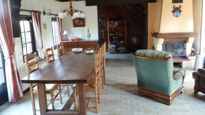 A dining area with a wooden table and chairs, a patterned armchair, and a fireplace. - Game room, fireplace and garden! (Le Faulq)