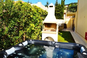 Relax in a serene outdoor space surrounded by lush greenery, featuring a hot tub and barbecue grill.