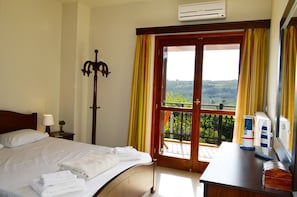 Relax in comfort with a large bed, a nightstand, and a chair, offering a serene view of the lush green landscape.