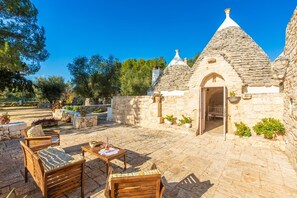 A stone building with a conical roof, a patio with wooden furniture, and potted plants. - Trullo with baby pool. NEAR THE SEA - PRIVACY - Fenced Garden - Yes pets - Wifi (San Vito Dei Normanni)