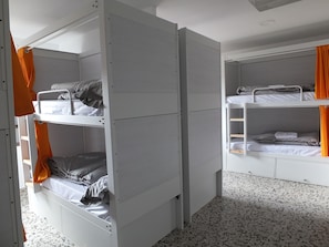 Ett sovsalsrum med våningssängar, en garderob och ett klinkergolv.
