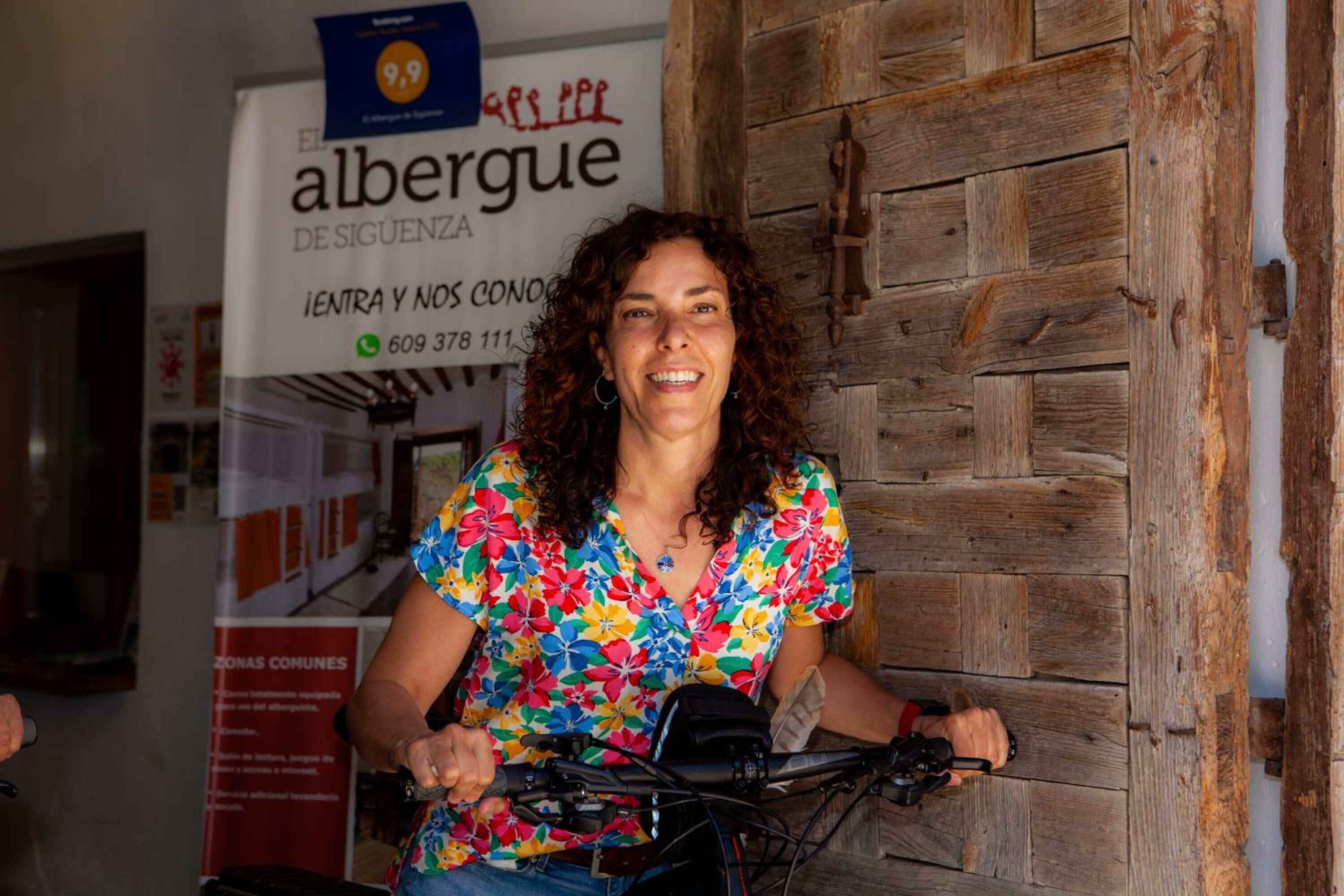 A person riding a bicycle in front of a wooden door with a sign that reads "albergue de seguimiento" and a phone number.