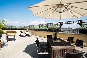 A rooftop terrace with a wooden table and chairs, a large umbrella, and a view of the city. - Rent holiday home Penthouse Panoramic terrace, historic center Rome (Roma)