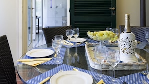 Una mesa de comedor dispuesta con platos, cubiertos, vasos, una botella y un frutero.