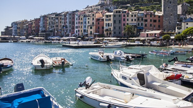 Un puerto deportivo con barcos amarrados, un pueblo histórico con edificios coloridos y un castillo en una colina.
