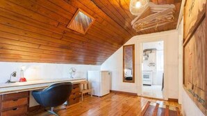 Accogliente camera da letto in mansarda con pavimento in legno, una scrivania con sedia, un piccolo frigorifero e vista sulla cucina.
