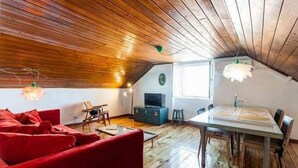 Una camera mansardata accogliente con travi in legno, un divano rosso, un tavolo da pranzo e una televisione.