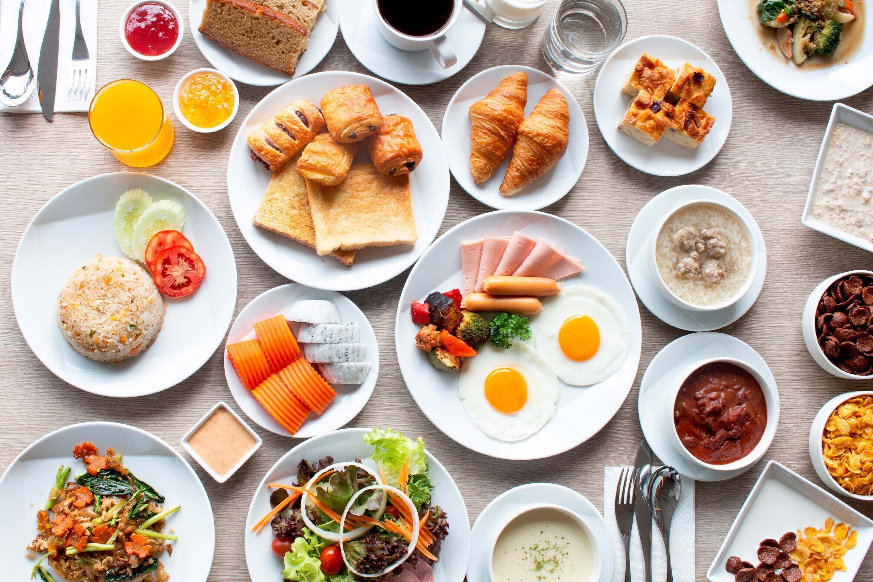 Variedad de platos para el desayuno, incluyendo cruasanes, huevos y tazones de arroz.