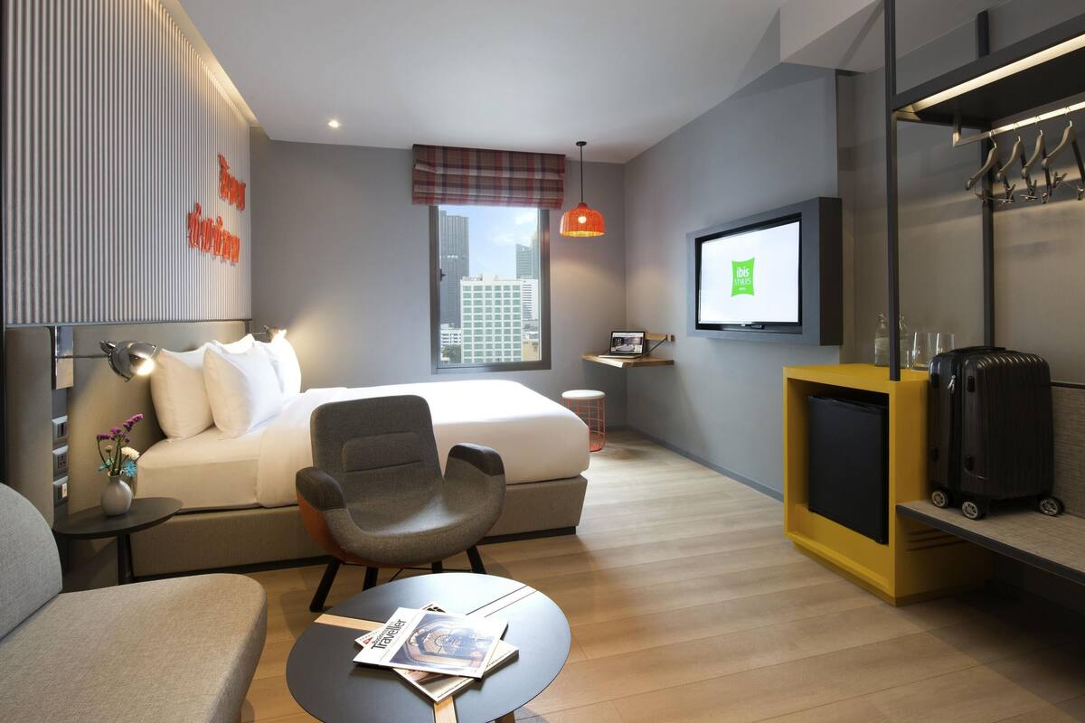 Habitación de hotel moderna con una cama, un escritorio, una silla, un televisor y vistas a la ciudad.