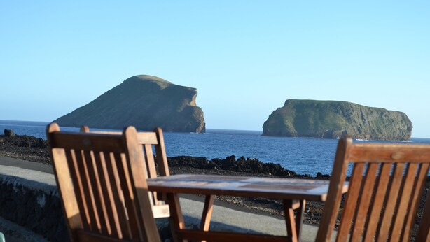 Une chaise et une table en bois, placées au bord d’une côte rocheuse, avec des falaises en arrière-plan.