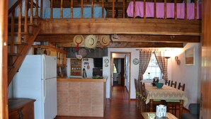 Une cuisine rustique avec un îlot central en briques, un escalier en bois et un coin repas comprenant une table et des chaises.