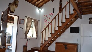 Un escalier en bois, un réfrigérateur blanc et un meuble en bois dans une pièce dont le sol est recouvert de carreaux.