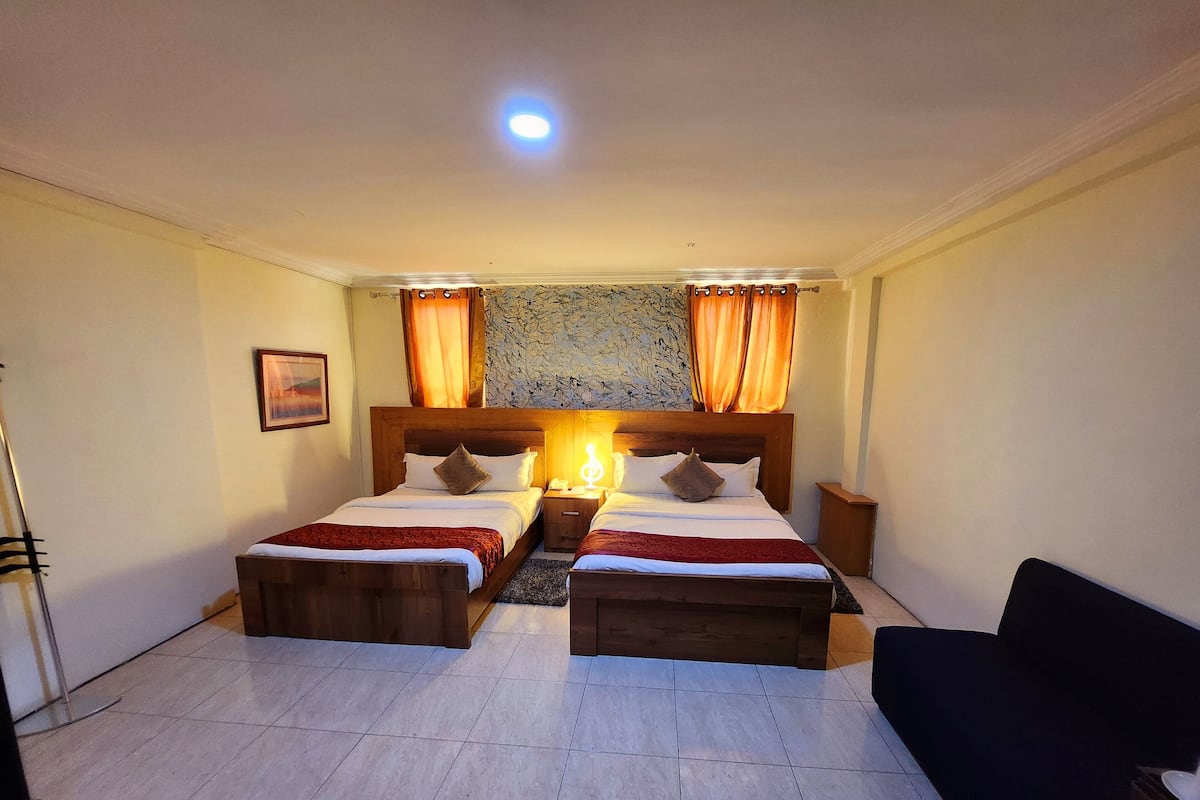 Une chambre d’hôtel avec deux lits, une table de chevet, une lampe, une chaise et un tableau au mur.