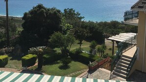A view of a balcony with a striped awning overlooking a garden and the ocean.