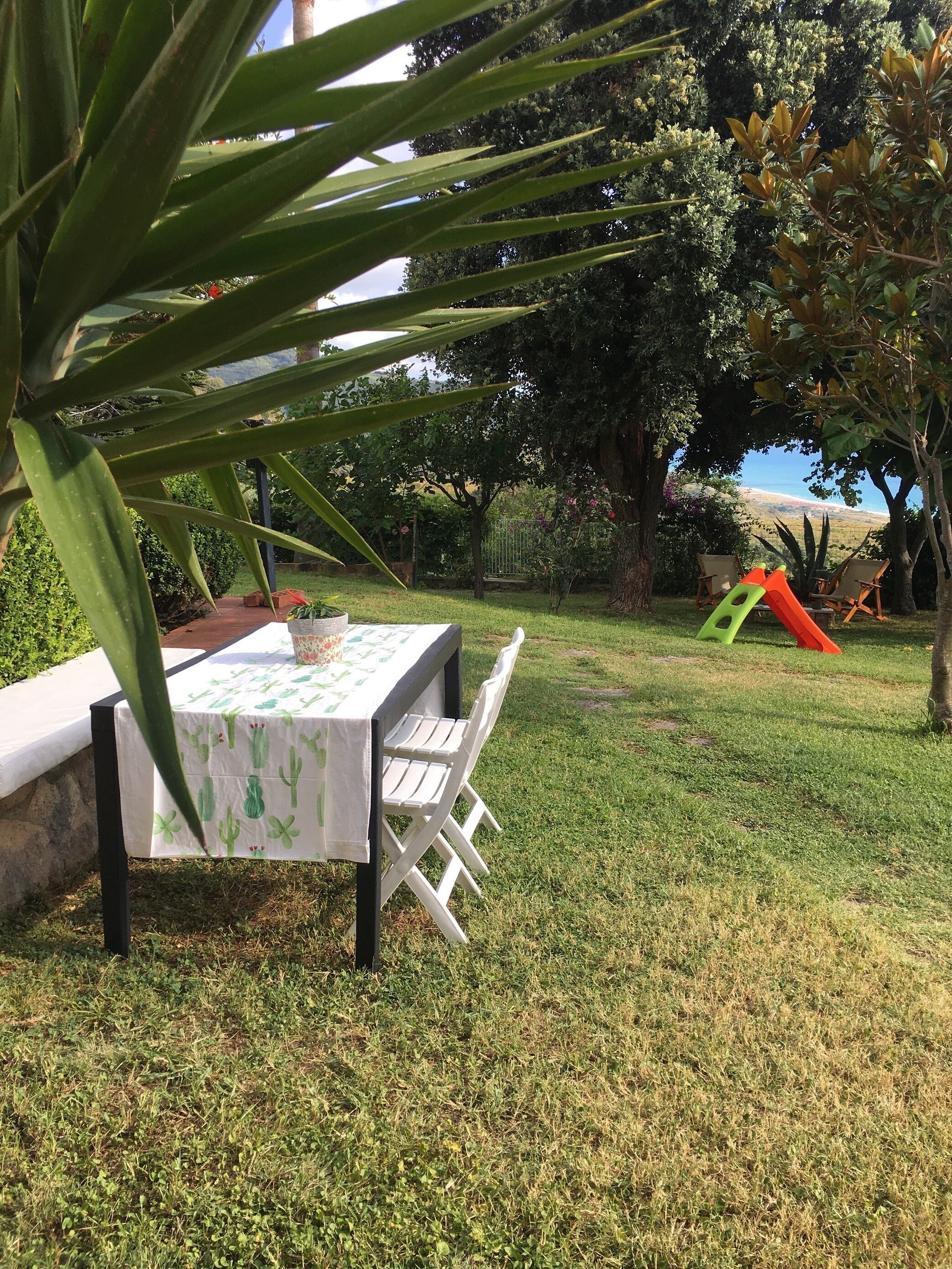 Un patio con mesa y sillas, rodeado de césped y árboles, con vistas al paisaje.
