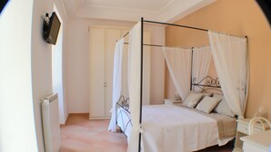 Una cama con dosel, ropa de cama blanca, una mesita de noche y un pequeño tocador.