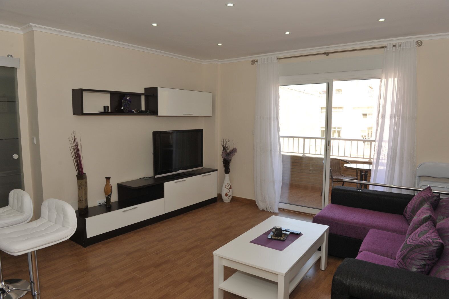 Ein modernes Wohnzimmer mit Flachbildfernseher, weißen Sofas, einem Couchtisch und einem Balkon mit Blick.