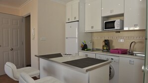 Cocina compacta con armarios blancos, microondas, cafetera y lavadora.