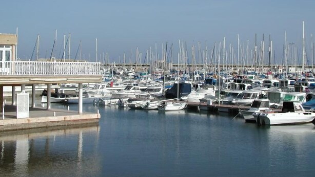 Un puerto deportivo con numerosas embarcaciones amarradas, un muelle y aguas tranquilas.